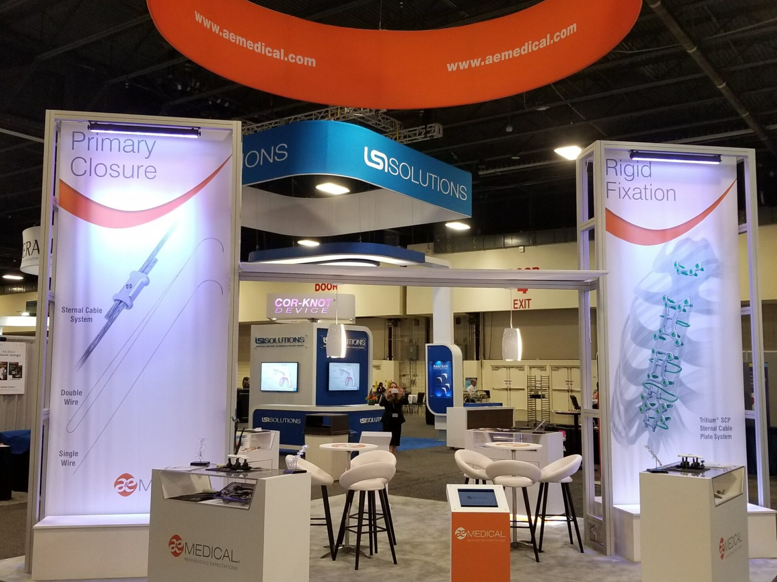 A&E Medical trade show booth at ready for show open. Large 20ft hanging ring with white on the outside and orange on the inside. 16ft metal towers with fabric graphics suspended on the interior.