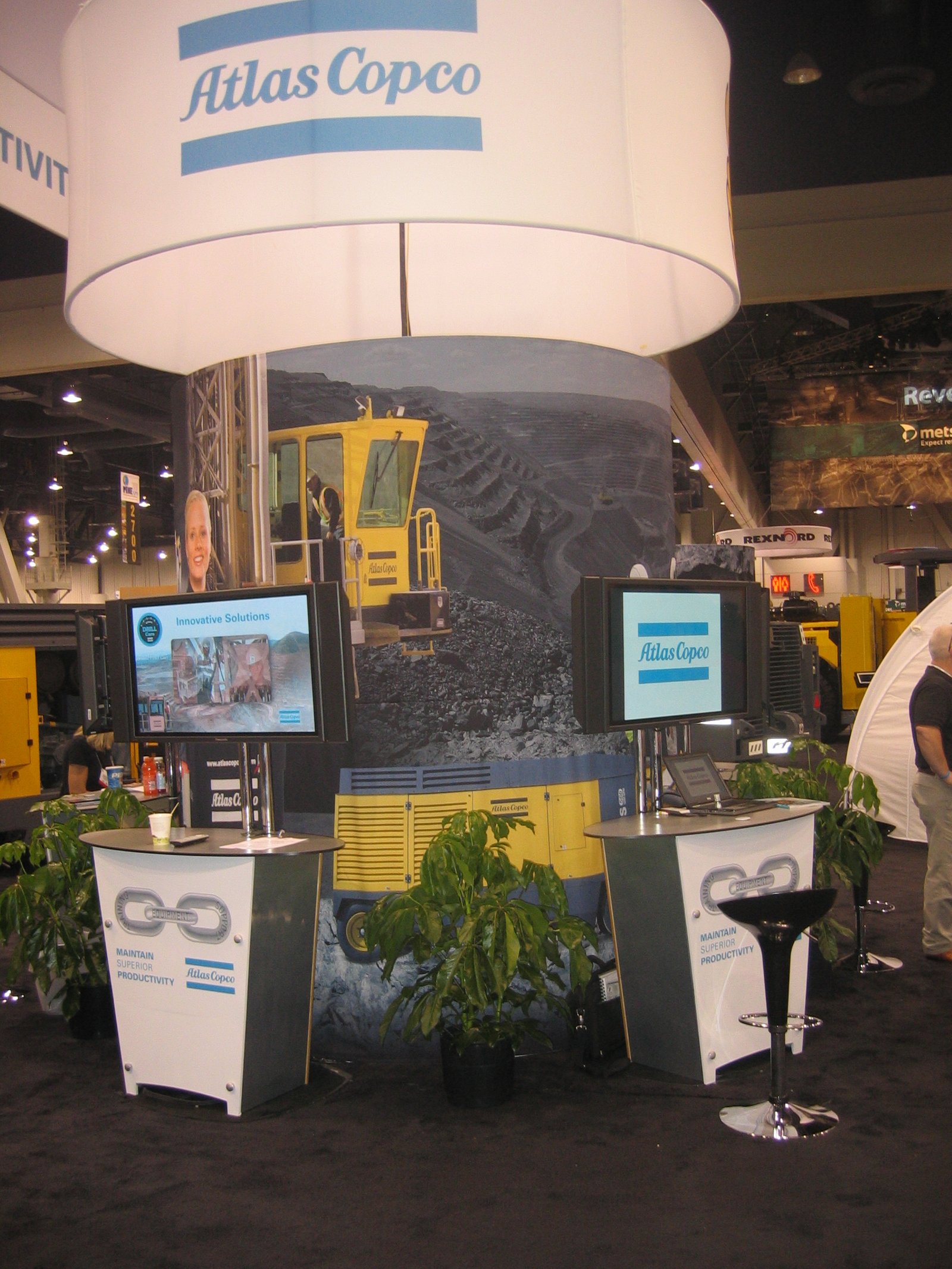 Closeup of Atlas Copco trade show display with large fabric cylinder printed with images of a large mine and trucks carrying ore. There is a white ring above this with an Atlas Copco teal logo.