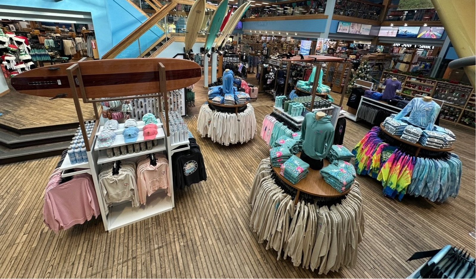 Ron Jon Surf Shop interior with racks of clothing and bamboo floor. Surfboard sits over top of clothing rack.