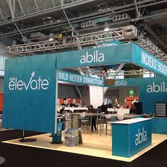 Abila 20x40 trade show booth with teal walls that levitate off the floor from suspended truss. The floor is a light color wood.