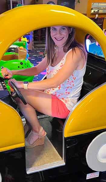 Woman smiling while sitting in a miniature car that serves as a ride for children.