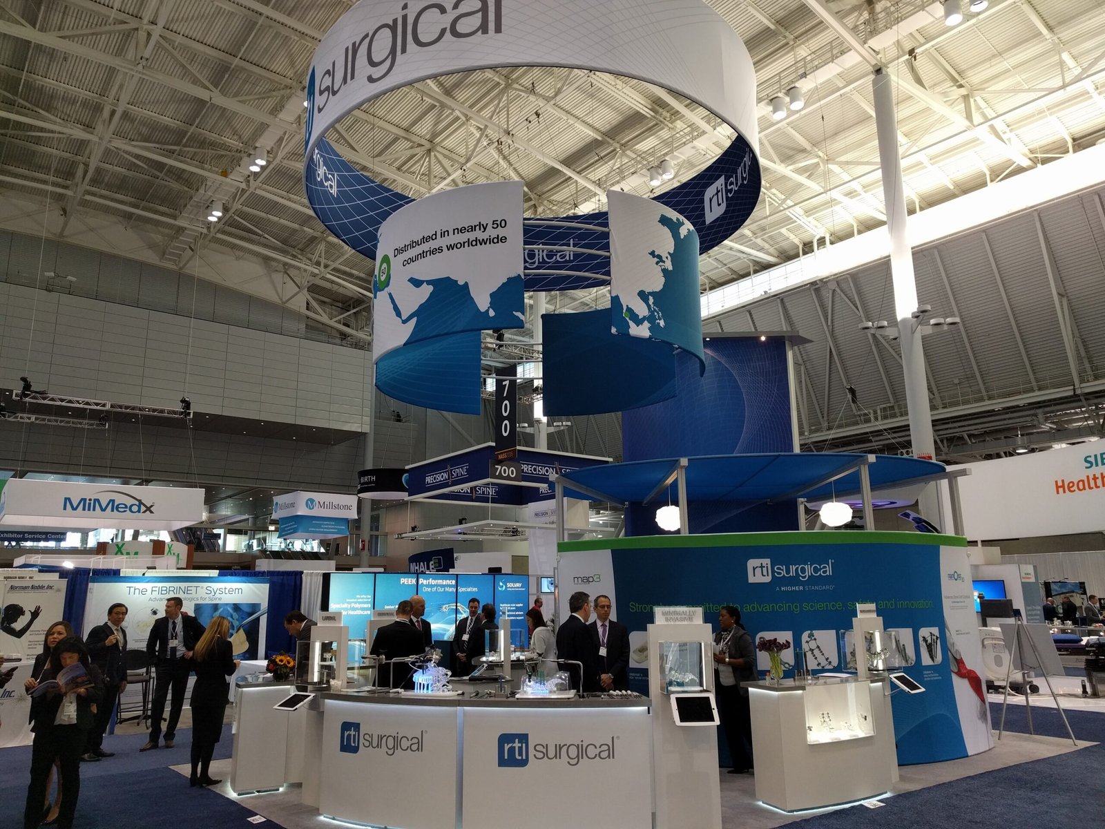 RTI Surgical 20x40 booth with white counters and large conference room and two ring hanging signs that read RTI Surgical. Colors are blue and white.