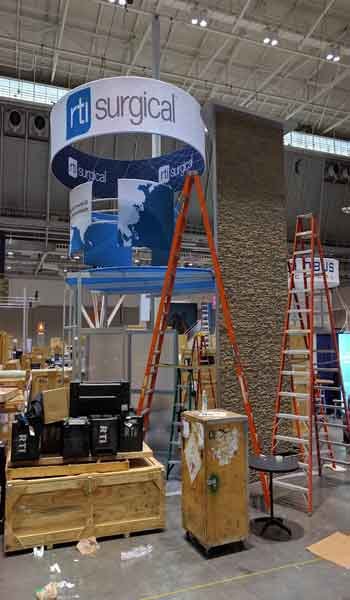 RTI Surgical 20x40 booth at a trade show under construction. Multiple ladders present.