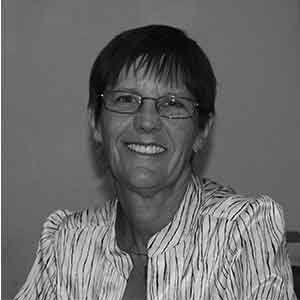 Black and white photo of Robbin Turner. She has short hair and is wearing glasses and a light colored striped shirt.