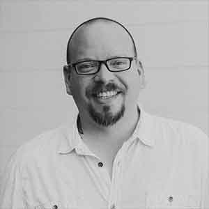 Black and white photo of Tim Carvalho. He is wearing glasses and a white collared shirt.